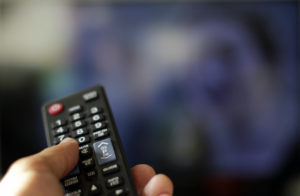 A hand holding a remote control presses buttons to switch TV channels