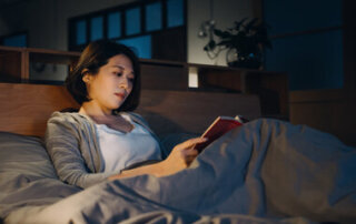 An Asian woman reading a book in bed at night
