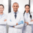 Five young physicians standing together, smiling, wearing white coats