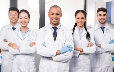 Five young physicians standing together, smiling, wearing white coats