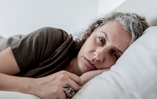 Person lying on their side in bed with eyes closed, resting on a pillow, suggesting sleep or fatigue.